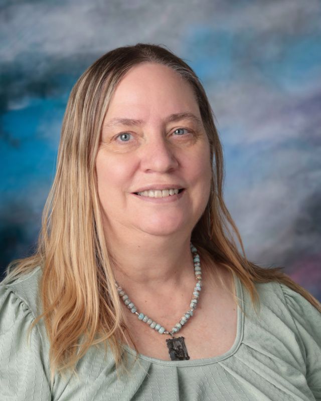 A woman in a green shirt is smiling in front of a blue background.