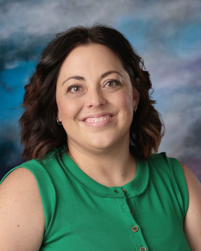 A woman in a green shirt is smiling in front of a blue background.