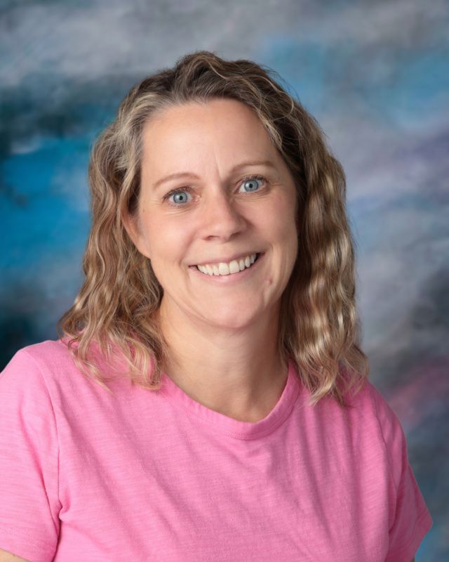 A woman in a black shirt is smiling in front of a blue background.