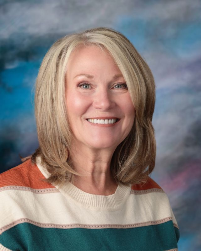 A woman in a blue jacket and black top is smiling for the camera.