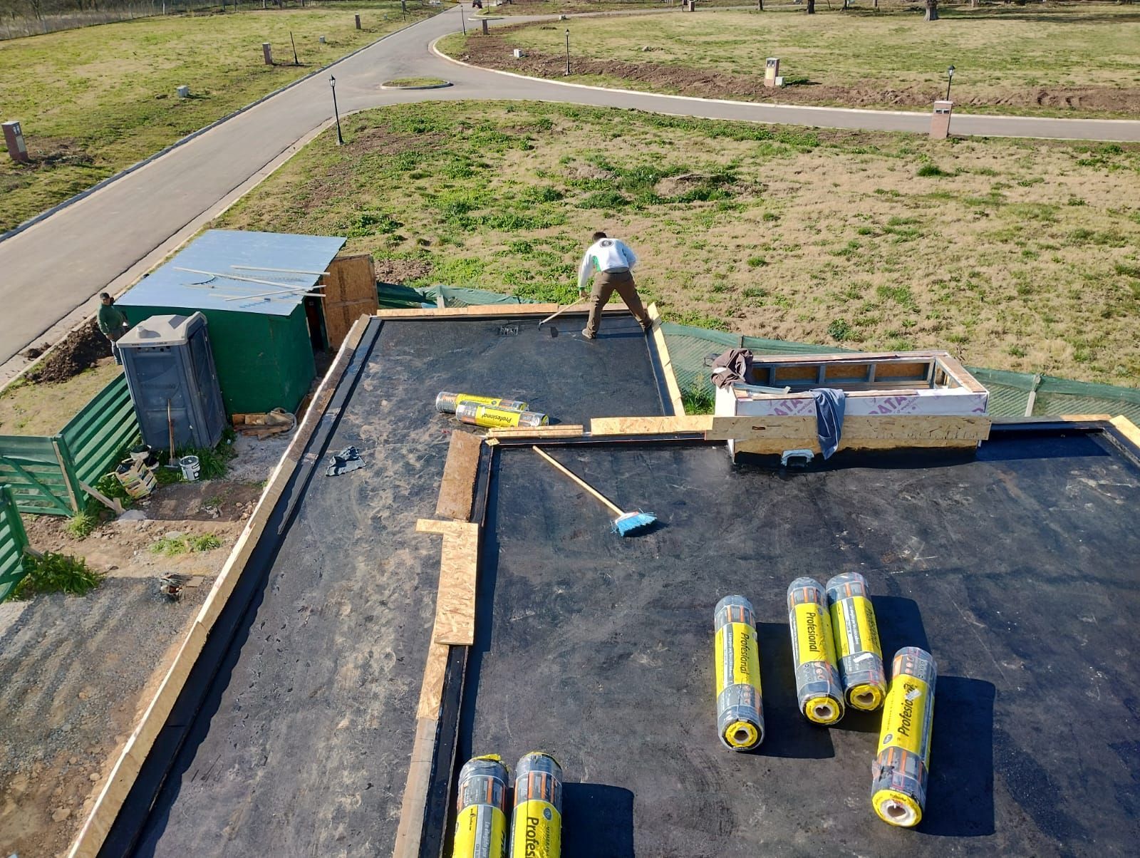 Materiales para techos y un trabajador en una azotea plana junto a una casa en construcción.