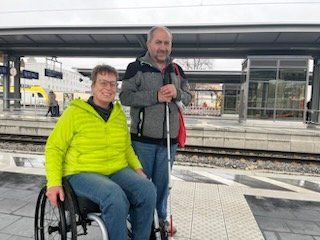 Eine Frau im Rollstuhl und ein Mann mit Langstock am Bahnsteig. Eine Frau im Rollstuhl und ein Mann mit Langstock am Bahnsteig.
