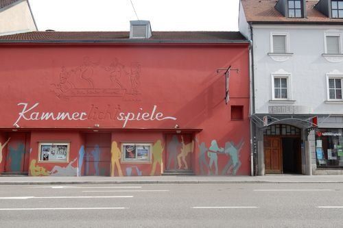 Kammerspiele Ansbach. Fensterloses längliches Gebäude, daneben mehrstöckiges Haus mit Torbogen. Kammerspiele Ansbach. Fensterloses längliches Gebäude, daneben mehrstöckiges Haus mit Torbogen.