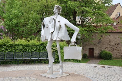 Überlebensgroße moderne Plastik Mann mit Koffer. Im Hintergrund Bäume und Stadtmauer. Überlebensgroße moderne Plastik Mann mit Koffer. Im Hintergrund Bäume und Stadtmauer.