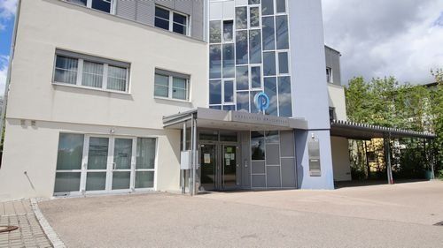 Schwabedastraße 1, mehrstöckiges Gebäude mit Anbau, davor Parkplatz