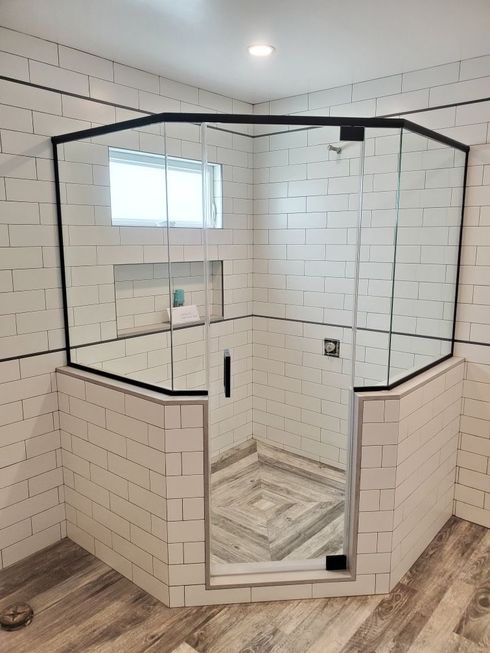 Glass shower enclosure with white subway tile walls and dark trim in a bathroom