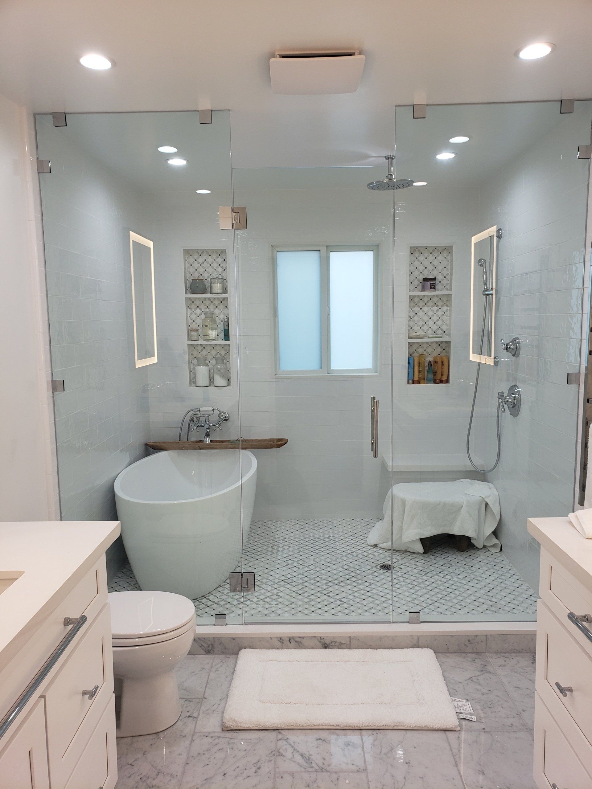 Bright modern bathroom with glass shower, freestanding tub, double vanity, and white tile floor.