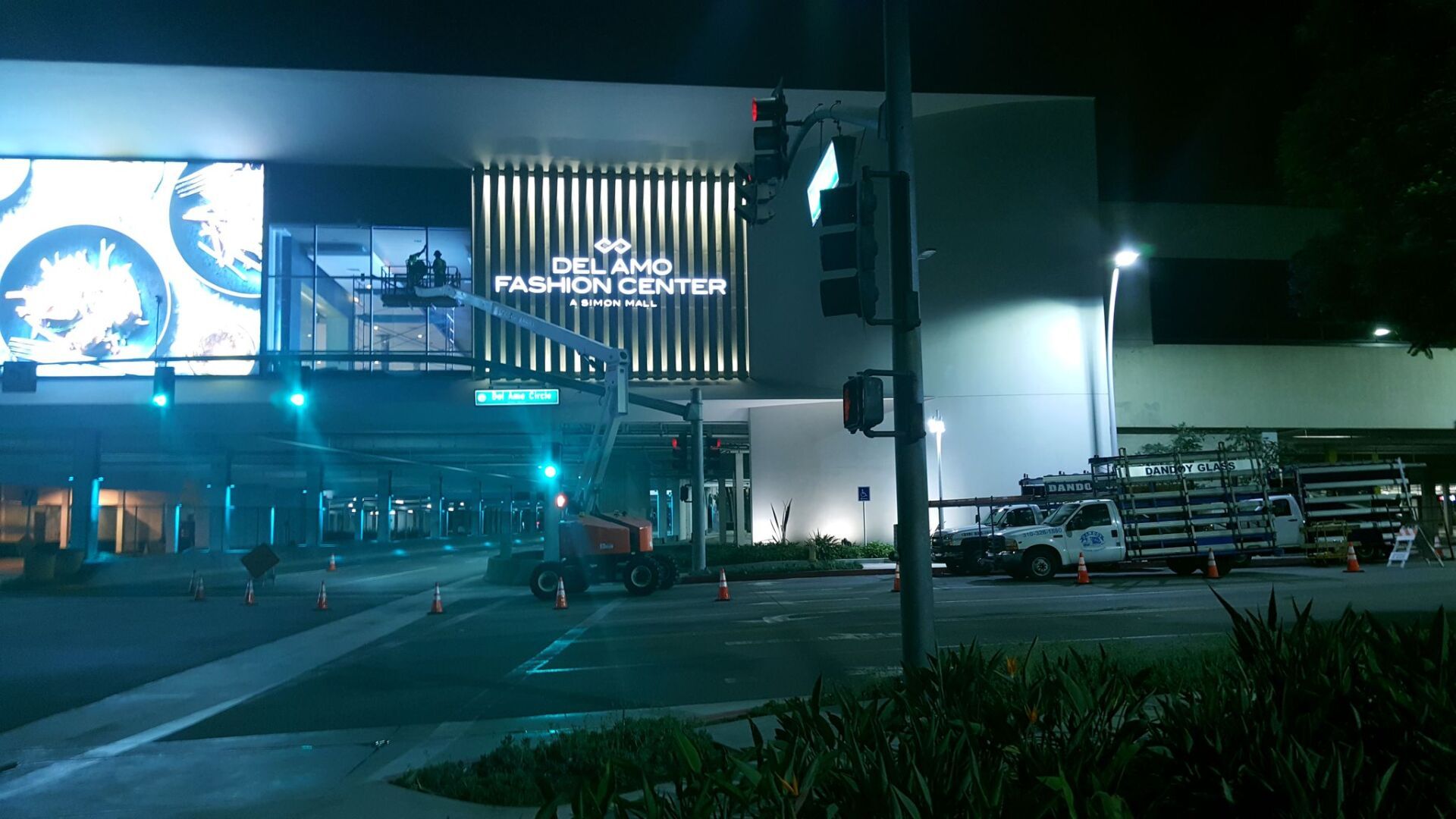 Nighttime view of a brightly lit shopping center with large illuminated signs and parked cars at the entrance Nighttime view of a brightly lit shopping center with large illuminated signs and parked cars at the entrance