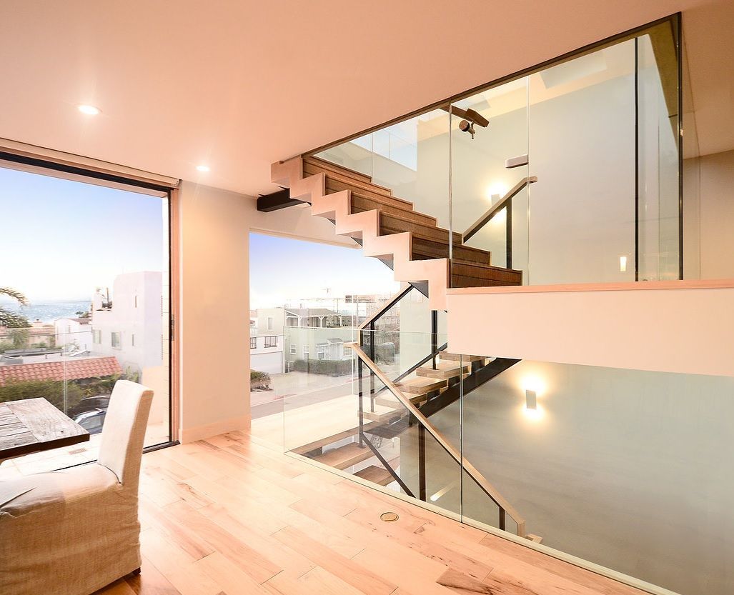 Modern interior with a floating wooden staircase beside a gray concrete wall and white rug runner Modern interior with floating staircase, glass railing, and large windows overlooking a bright view