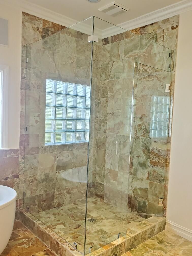 Glass-enclosed tiled shower stall with mosaic stone walls and a built-in bench