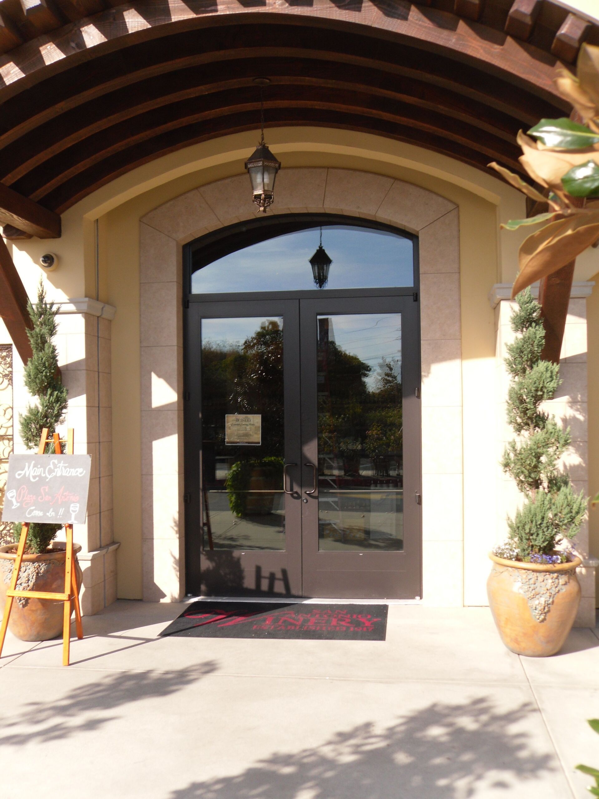 Arched storefront entrance with glass double doors, potted plants, and a welcome mat under a covered awning Arched storefront entrance with glass double doors, potted plants, and a welcome mat under a covered awning
