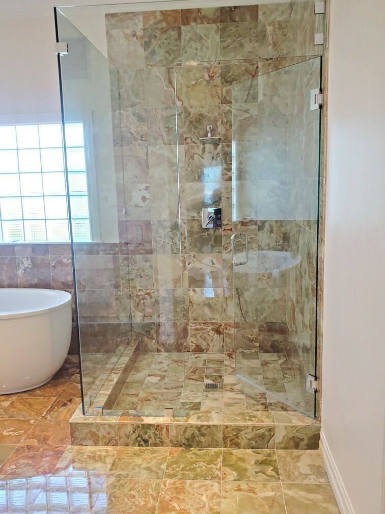 Glass walk-in shower with beige stone tile in a bright bathroom