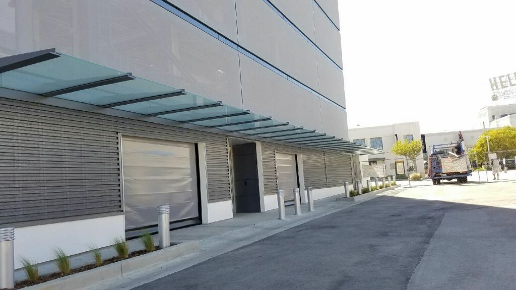 Modern building entrance with glass awning, ramp, and empty paved driveway on a sunny day Modern building entrance with glass awning, ramp, and empty paved driveway on a sunny day