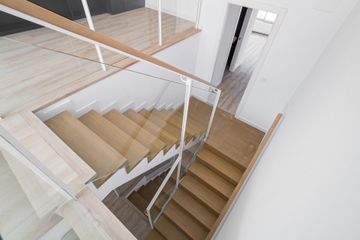 Modern interior staircase with wooden steps, glass railing, and white walls, viewed from above