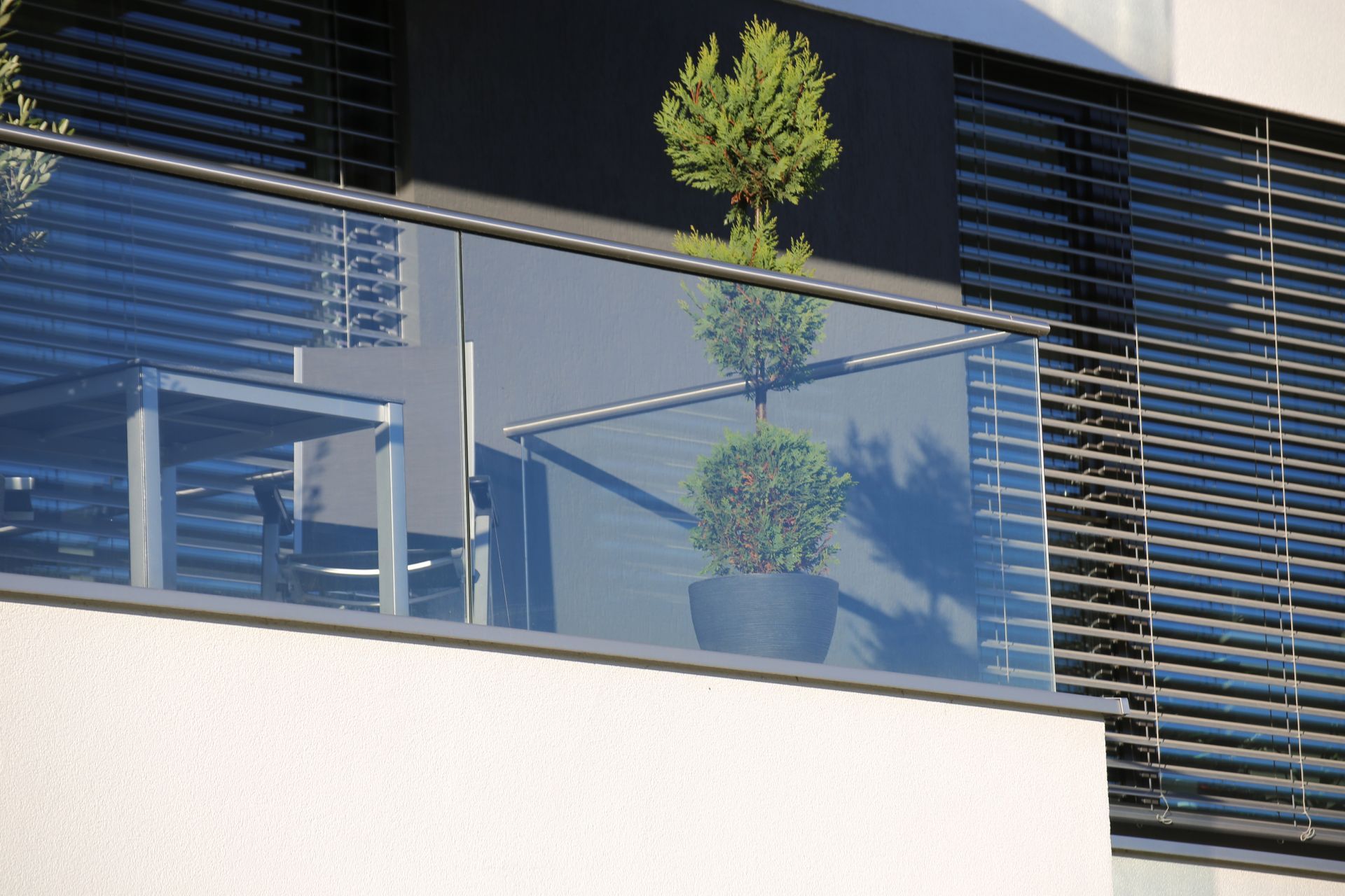 Modern balcony with glass railing, potted plants, and dark horizontal slats on a contemporary building