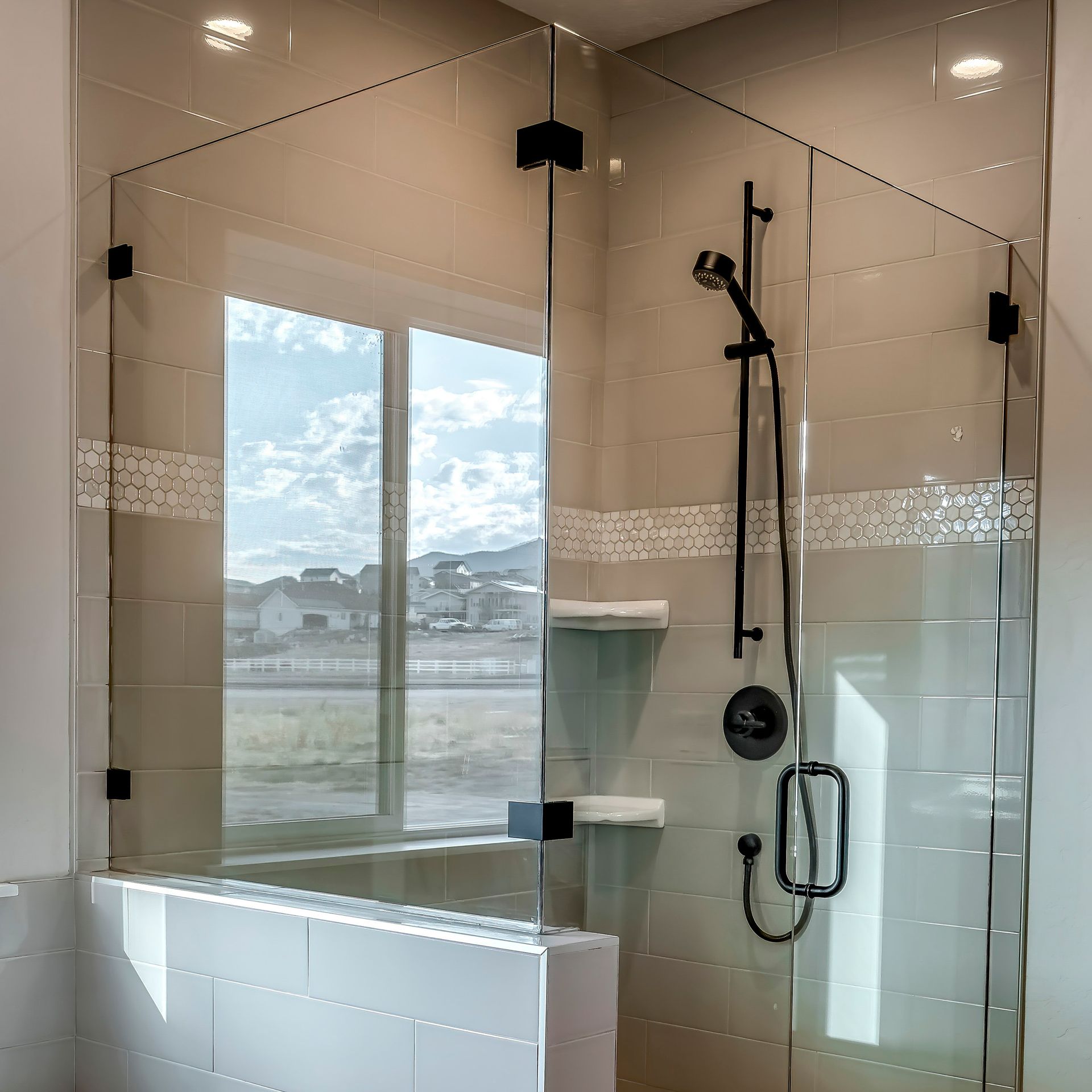 Glass walk-in shower with white tub, chrome fixtures, and a window overlooking a snowy landscape