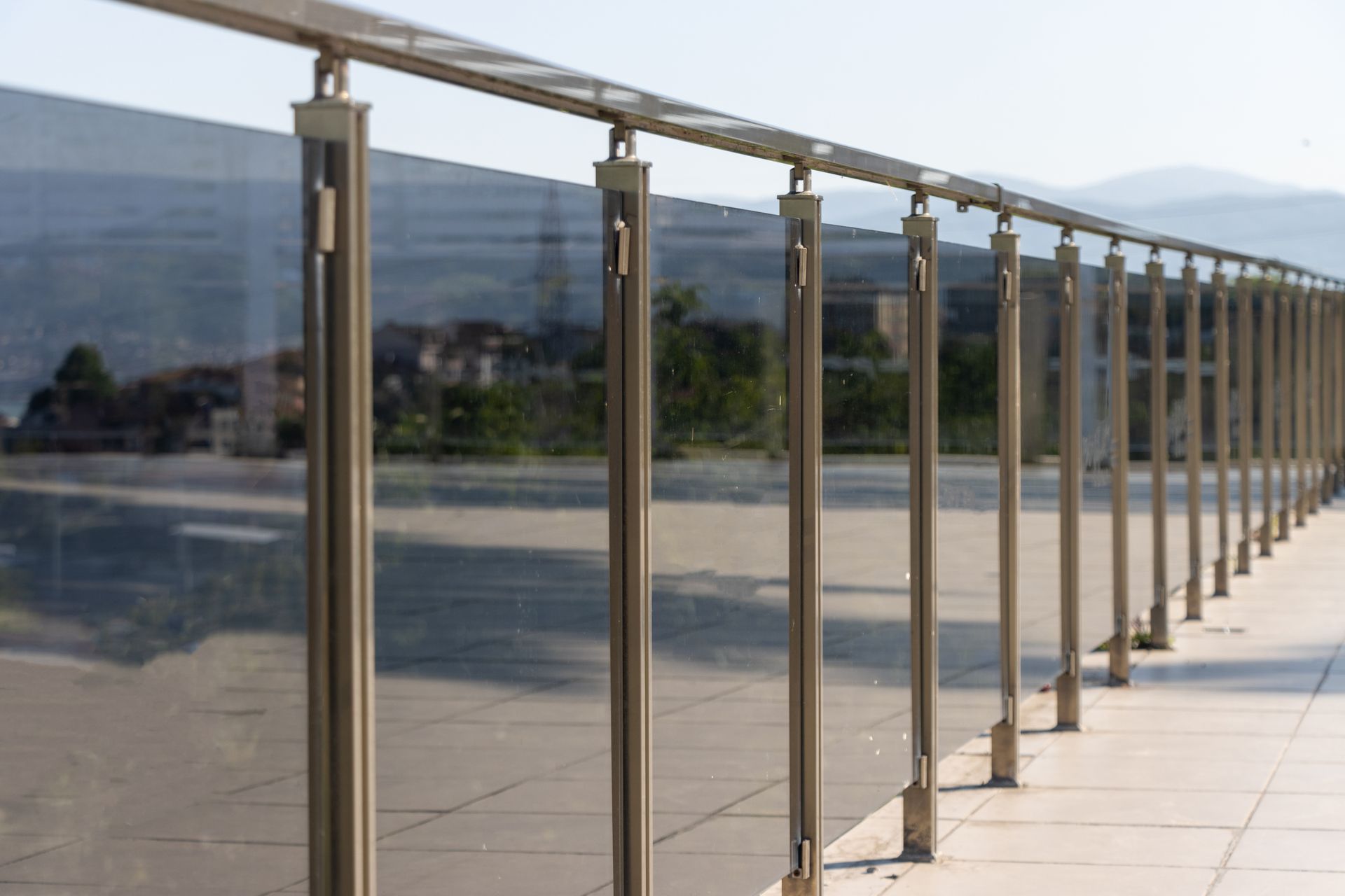 Glass railing along a sunlit terrace with mountain views in the distance