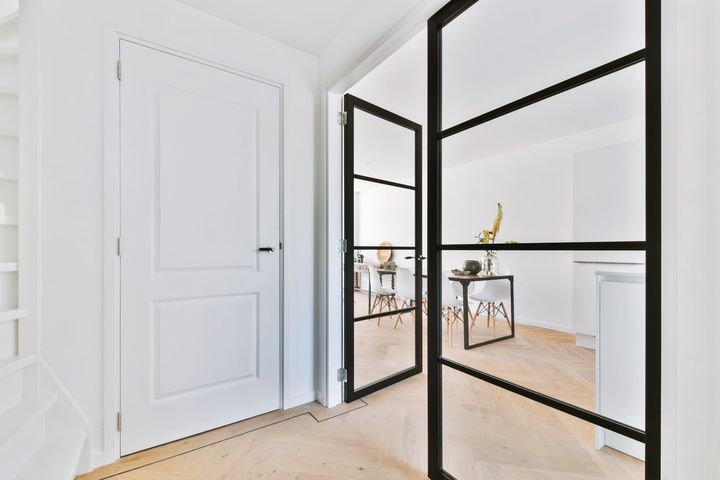 Bright hallway with white doors, black-framed mirrors, and light wood flooring in a minimalist interior