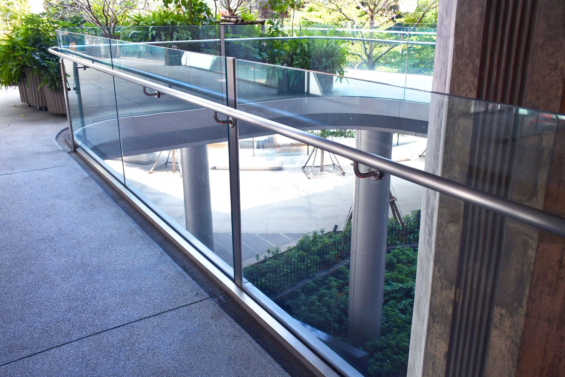 Glass-railed outdoor walkway beside a modern building and landscaped area
