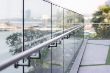 Glass-railed walkway overlooking a calm waterfront on a bright day