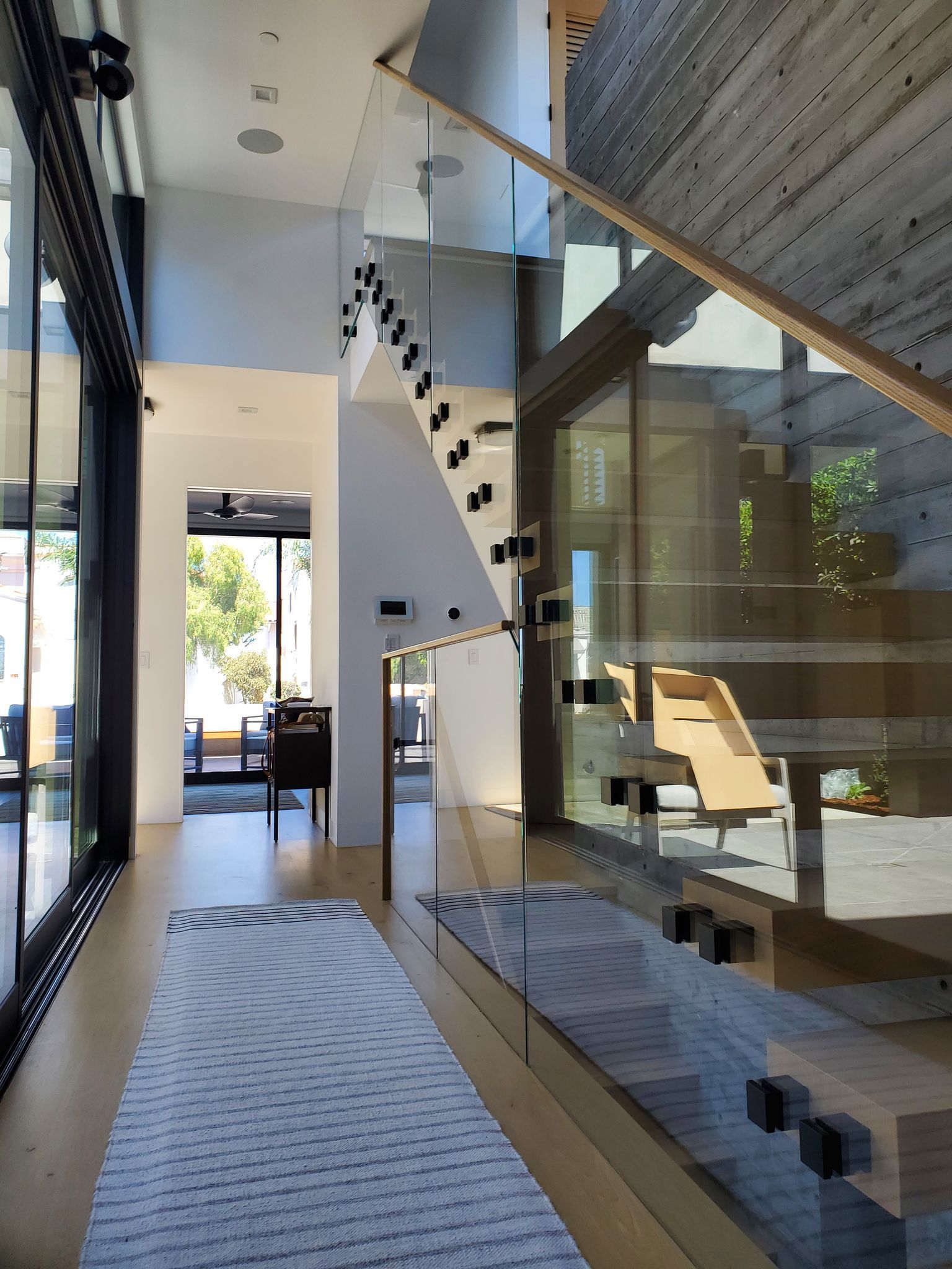 Modern home interior with glass wall, staircase, lounge chair, and patterned rug on a bright hallway Modern home interior with glass wall, staircase, lounge chair, and patterned rug on a bright hallway