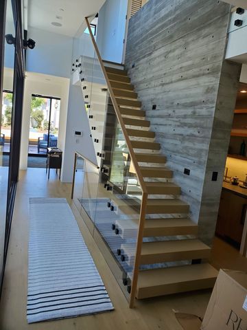 Modern interior with a floating wooden staircase beside a gray concrete wall and white rug runner
