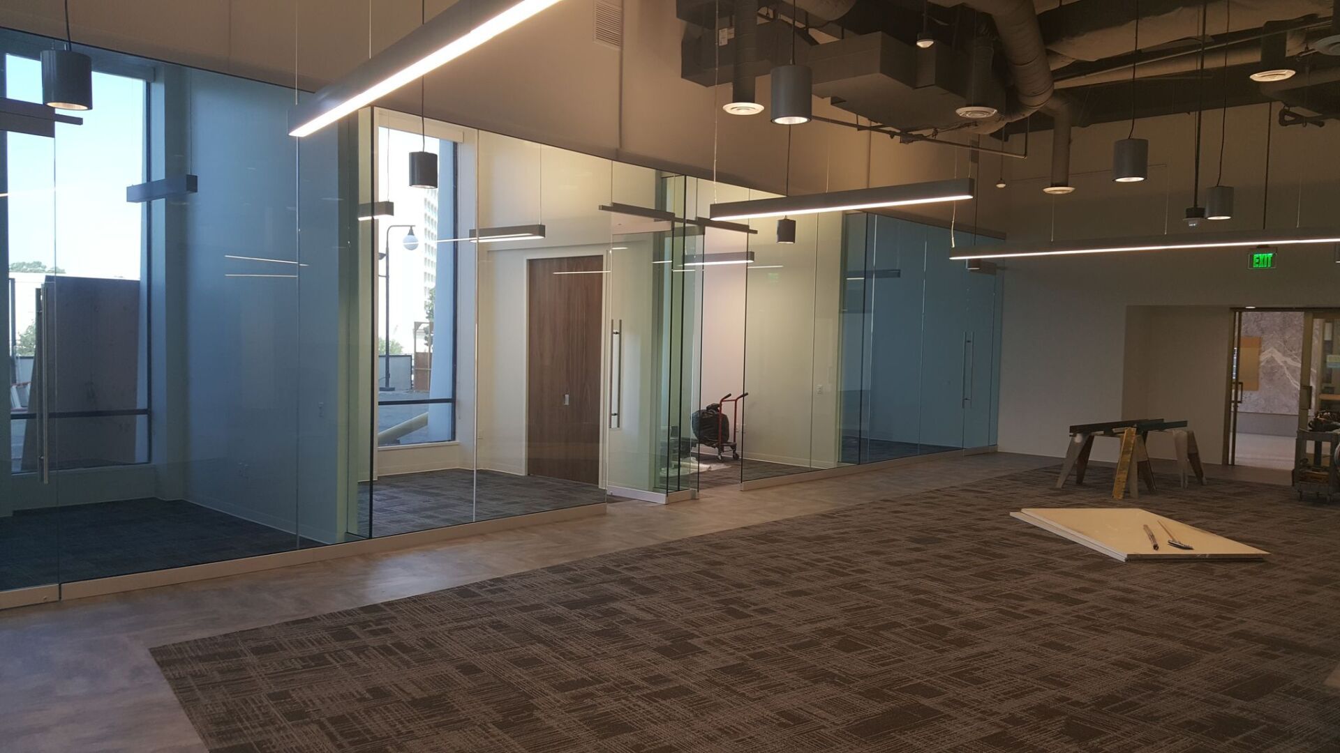 Empty modern office space with glass walls, exposed ceiling, carpeted floor, and a white table near the center Empty modern office space with glass walls, exposed ceiling, carpeted floor, and a white table near the center
