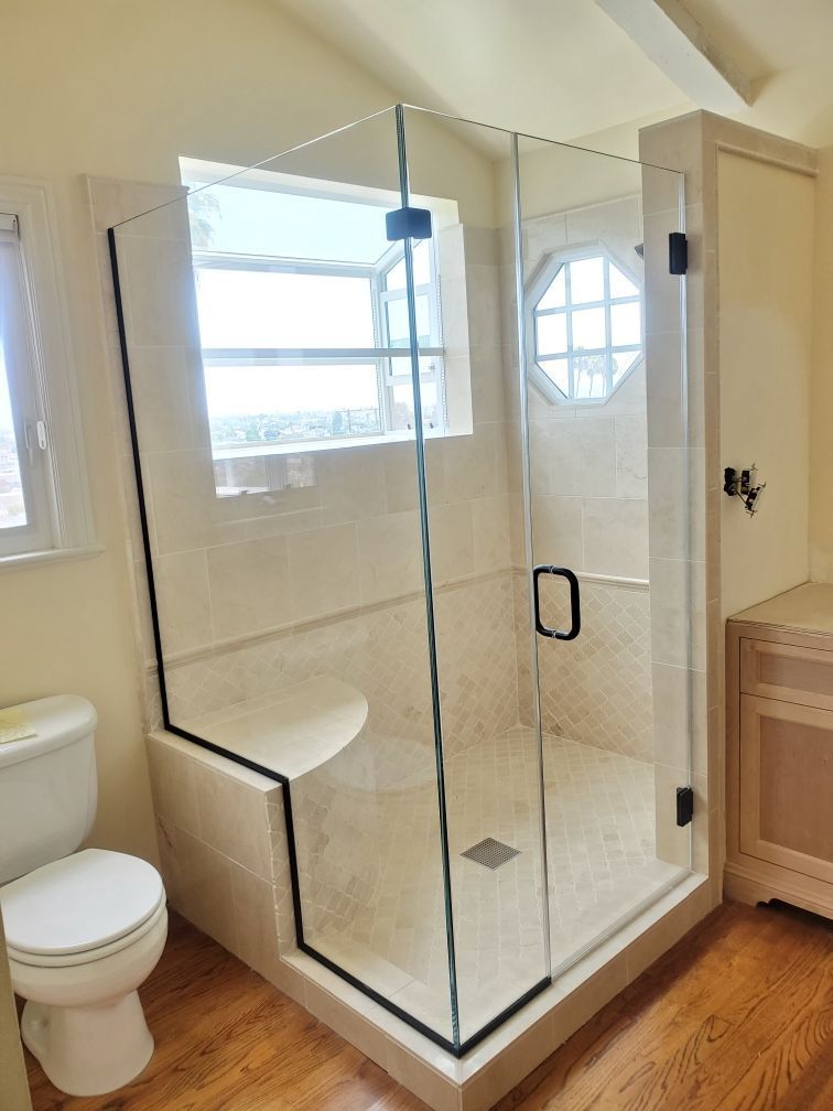 Glass walk-in shower with beige tile, black trim, and adjacent toilet and wood vanity in a bathroom