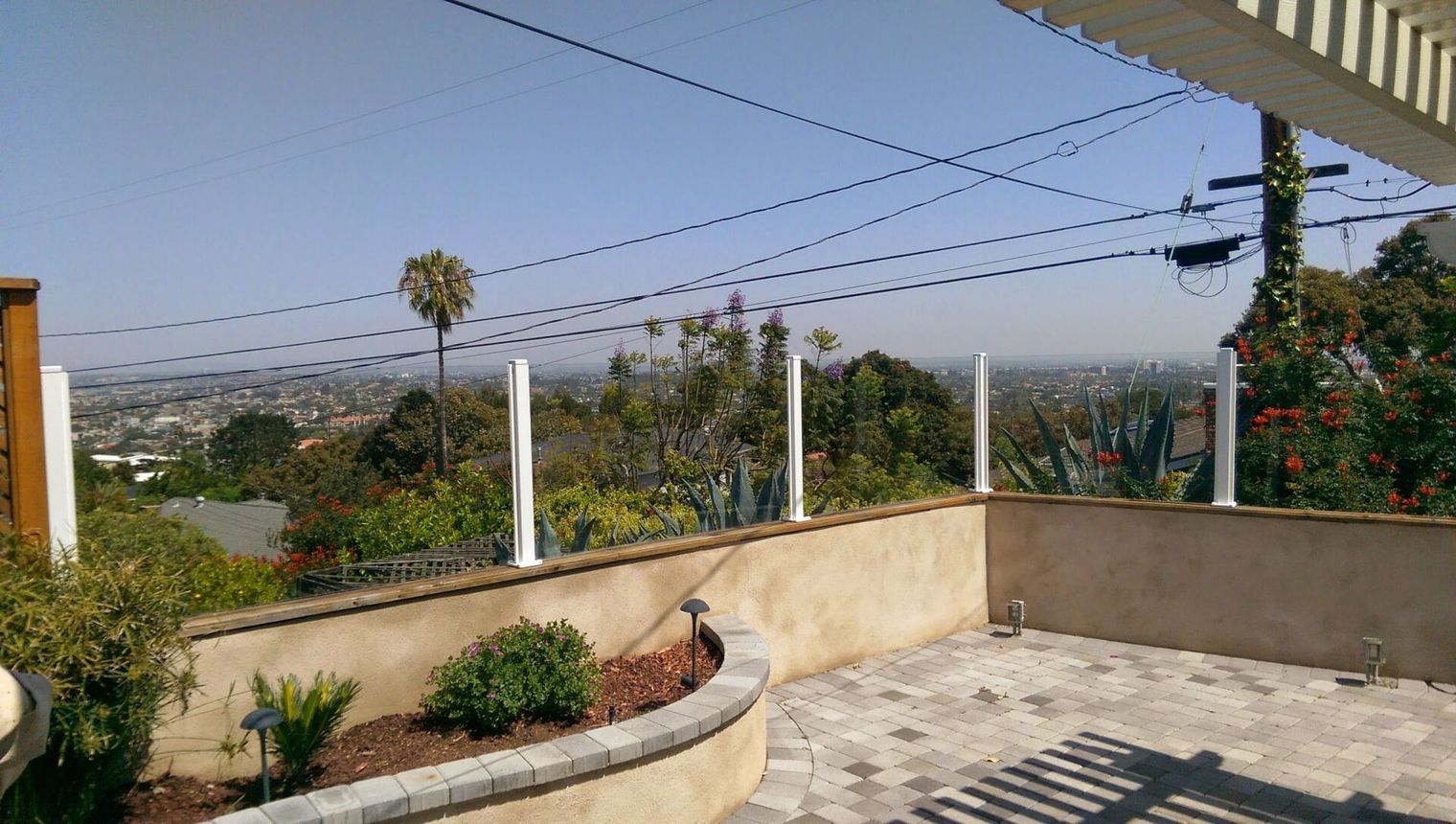 Sunny rooftop patio with curved planter, palm trees, and distant city view under power lines
