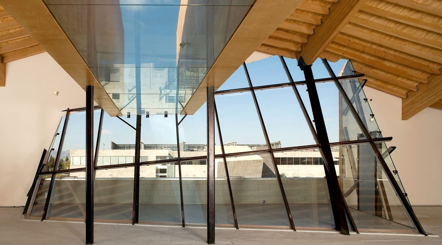 Modern pavilion interior with slanted black columns, glass ceiling, and wooden beams overlooking an open plaza Modern pavilion interior with slanted black columns, glass ceiling, and wooden beams overlooking an open plaza