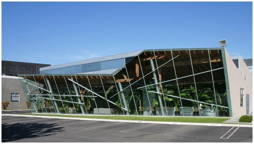 Modern glass-fronted building with slanted facade and reflective windows under a clear blue sky Modern glass-fronted building with slanted facade and reflective windows under a clear blue sky