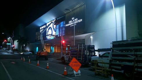 Nighttime street view of a lit storefront with cones and a roadwork sign outside.