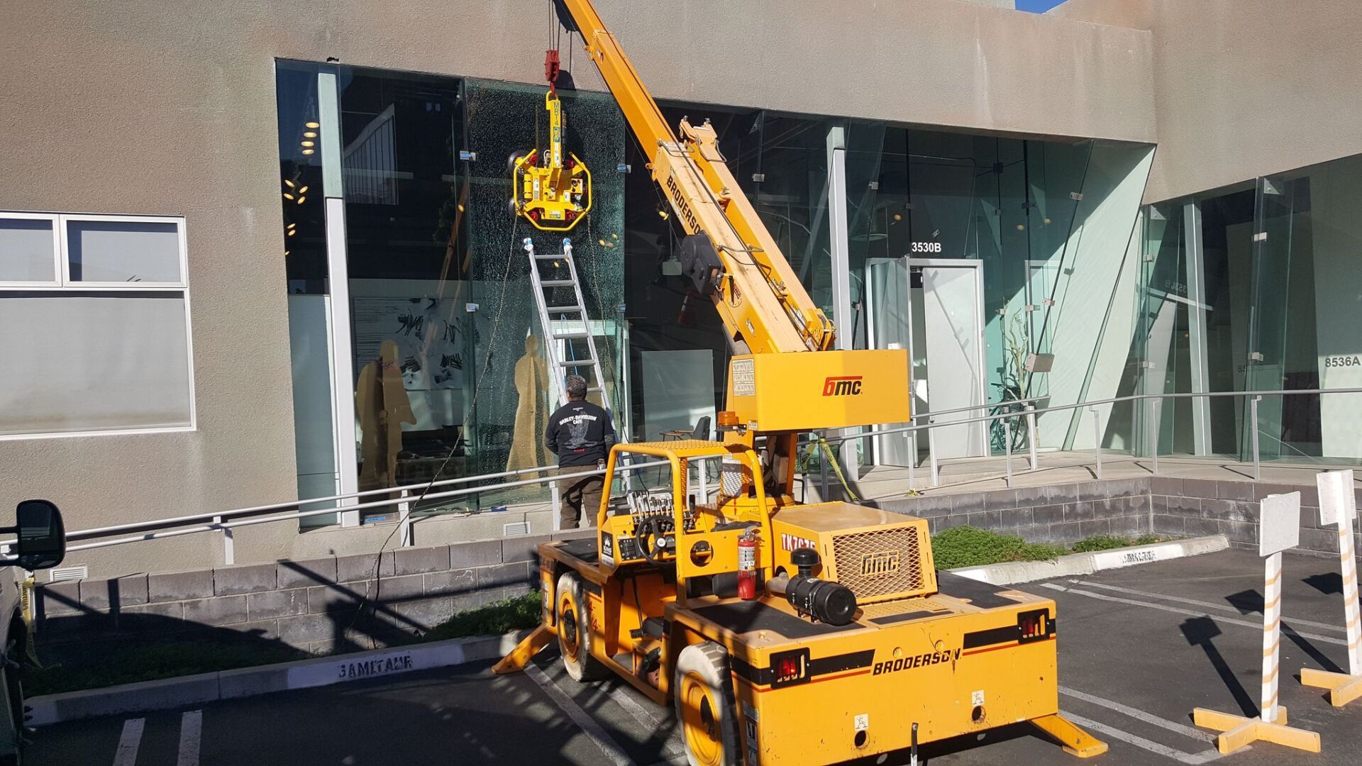 Yellow crane lifting a black cylindrical load outside a glass-fronted building Yellow crane lifting a black cylindrical load outside a glass-fronted building