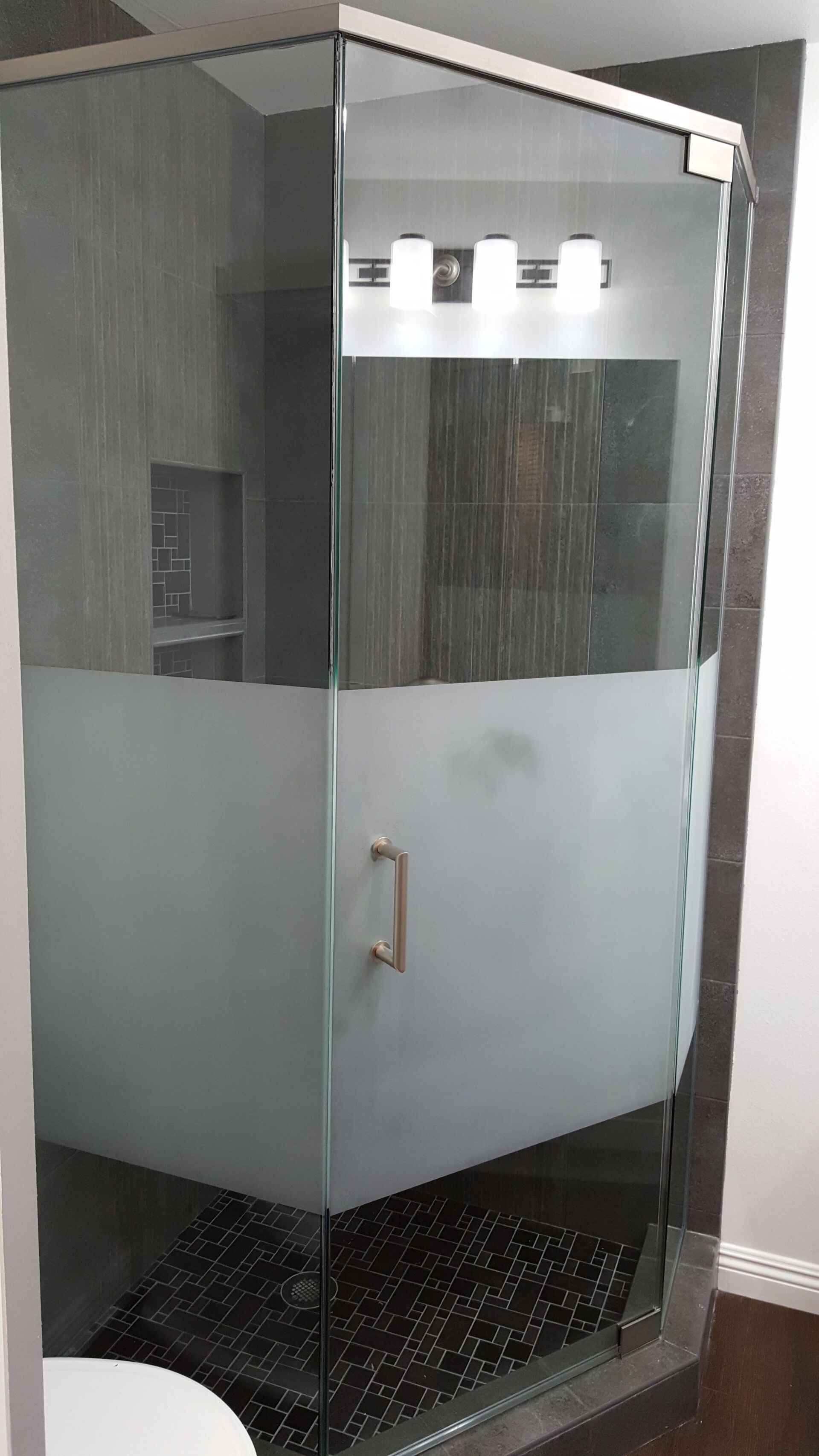 Glass shower stall with frosted lower panels and black tile floor in a bathroom