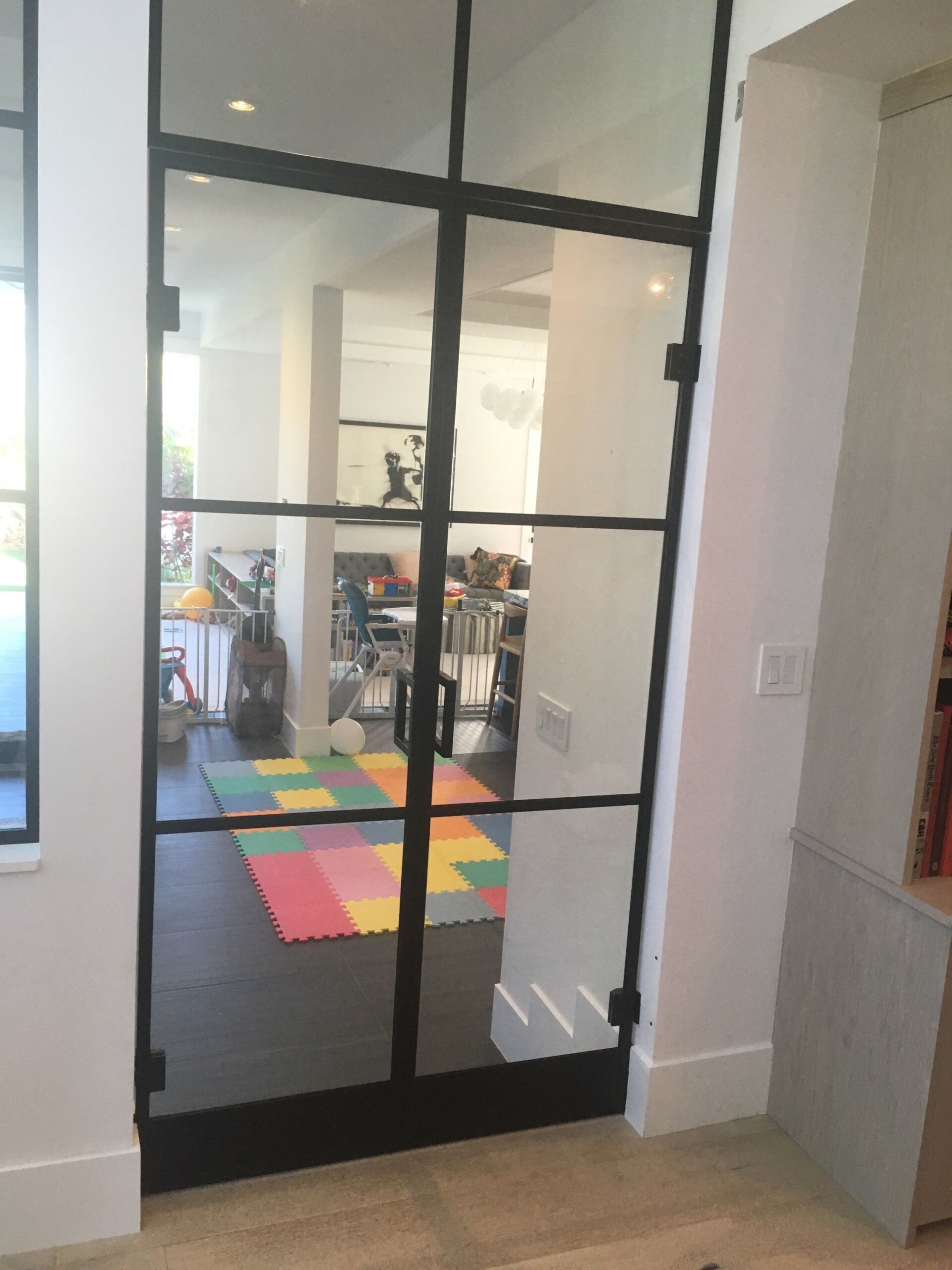 Black-framed glass door opening to a playroom with colorful foam mats and toys inside Black-framed glass door opening to a playroom with colorful foam mats and toys inside