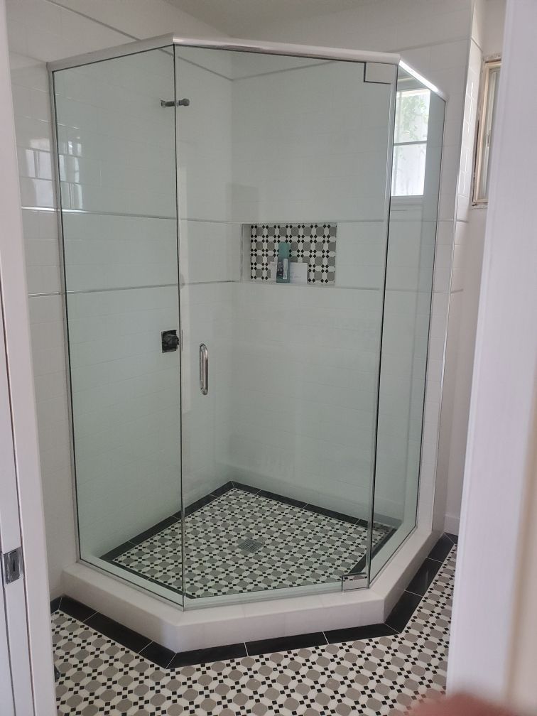 Glass shower enclosure with white tiled walls and patterned floor in a bathroom