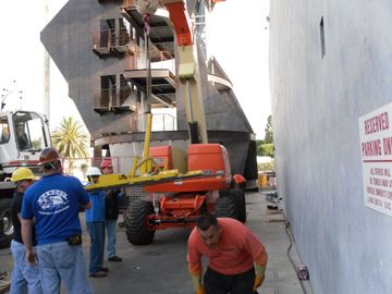 Construction workers on a lift beside a large ship hull in a dry dock