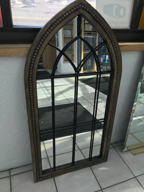 Tall arched decorative mirror with dark frame leaning against a wall on a tiled floor Tall arched decorative mirror with dark frame leaning against a wall on a tiled floor