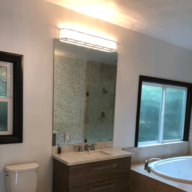 Modern bathroom with a vanity, illuminated mirror, toilet, and a tub beside a window. Modern bathroom with a vanity, illuminated mirror, toilet, and a tub beside a window.