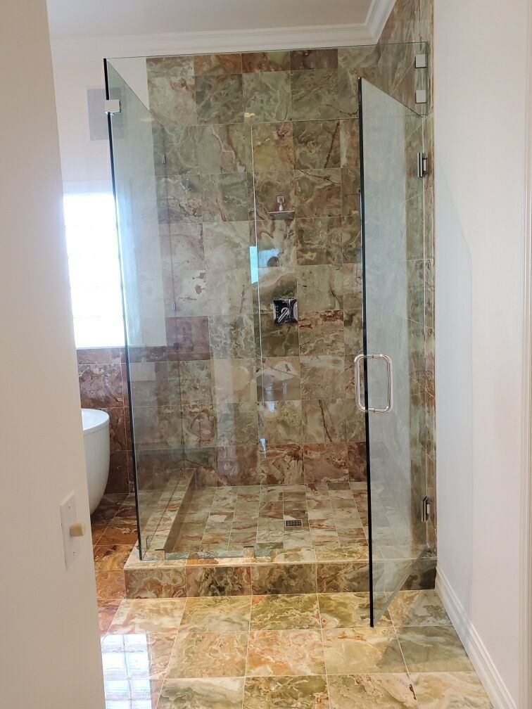 Glass walk-in shower with stone tile walls and floor in a bathroom