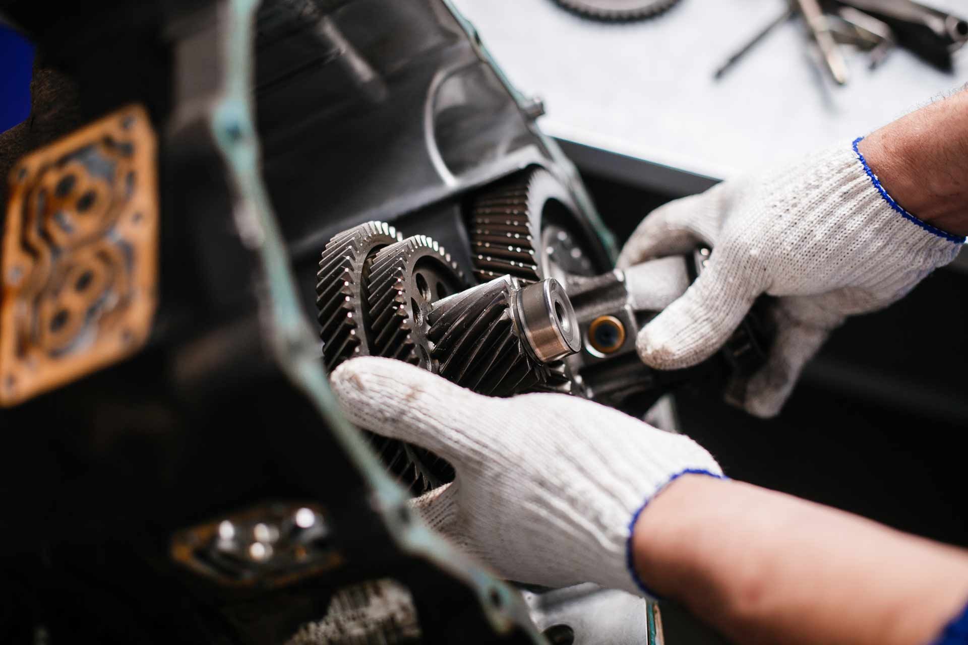 Hands in white gloves repairing a metal watch mechanism with gears and tools