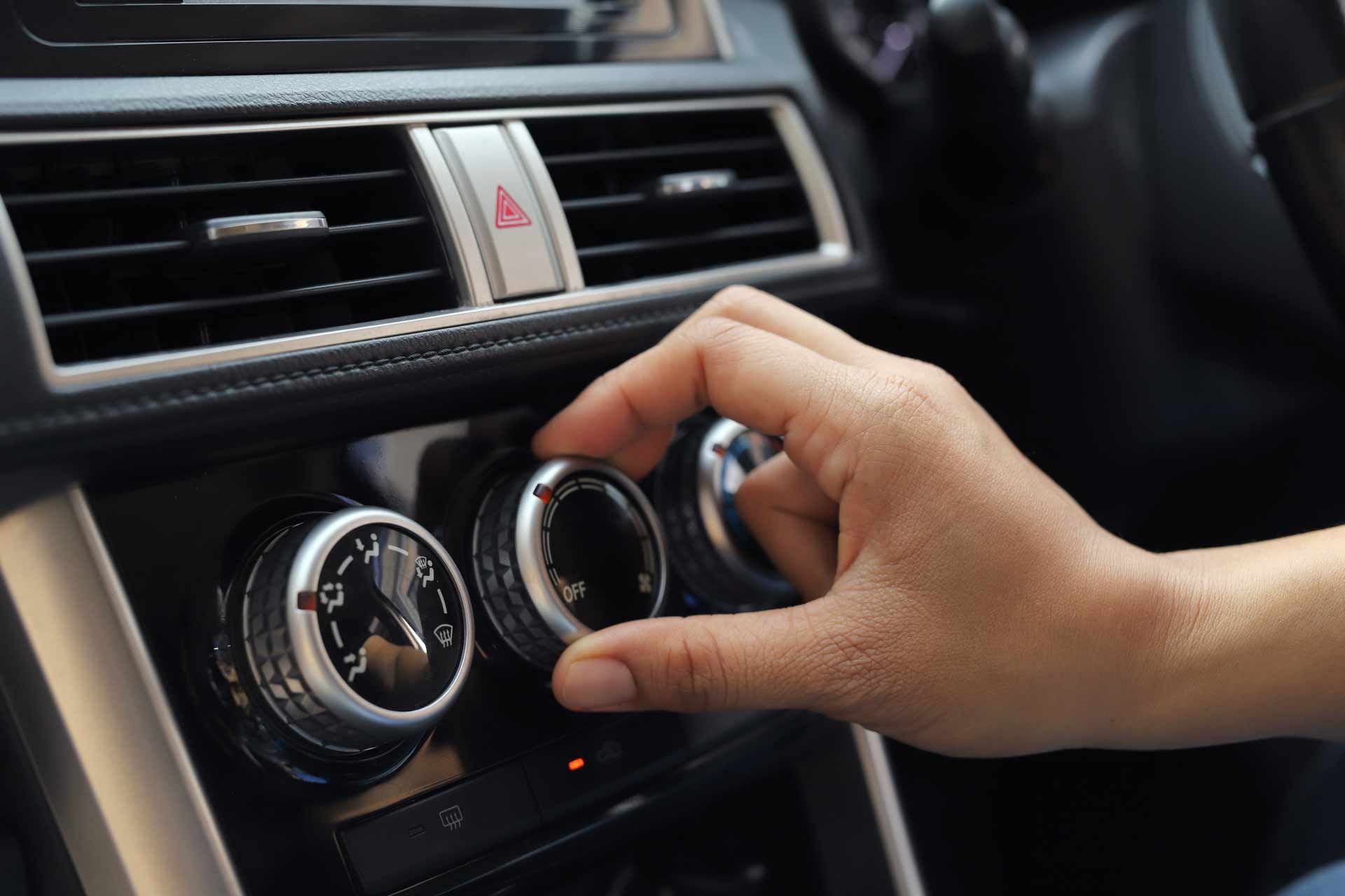 Hand adjusting a car’s climate control knobs on the dashboard.