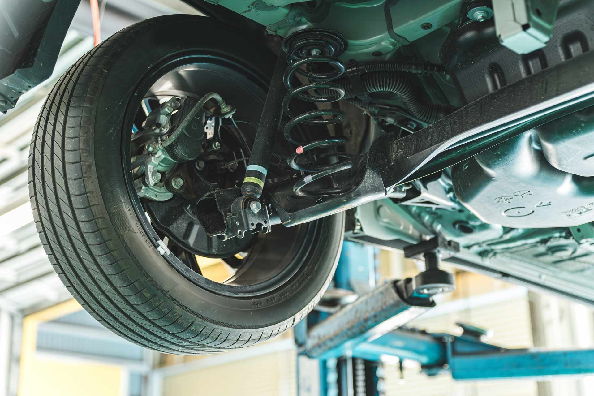 Car’s undercarriage on a lift, showing rear suspension and tire in an auto repair shop