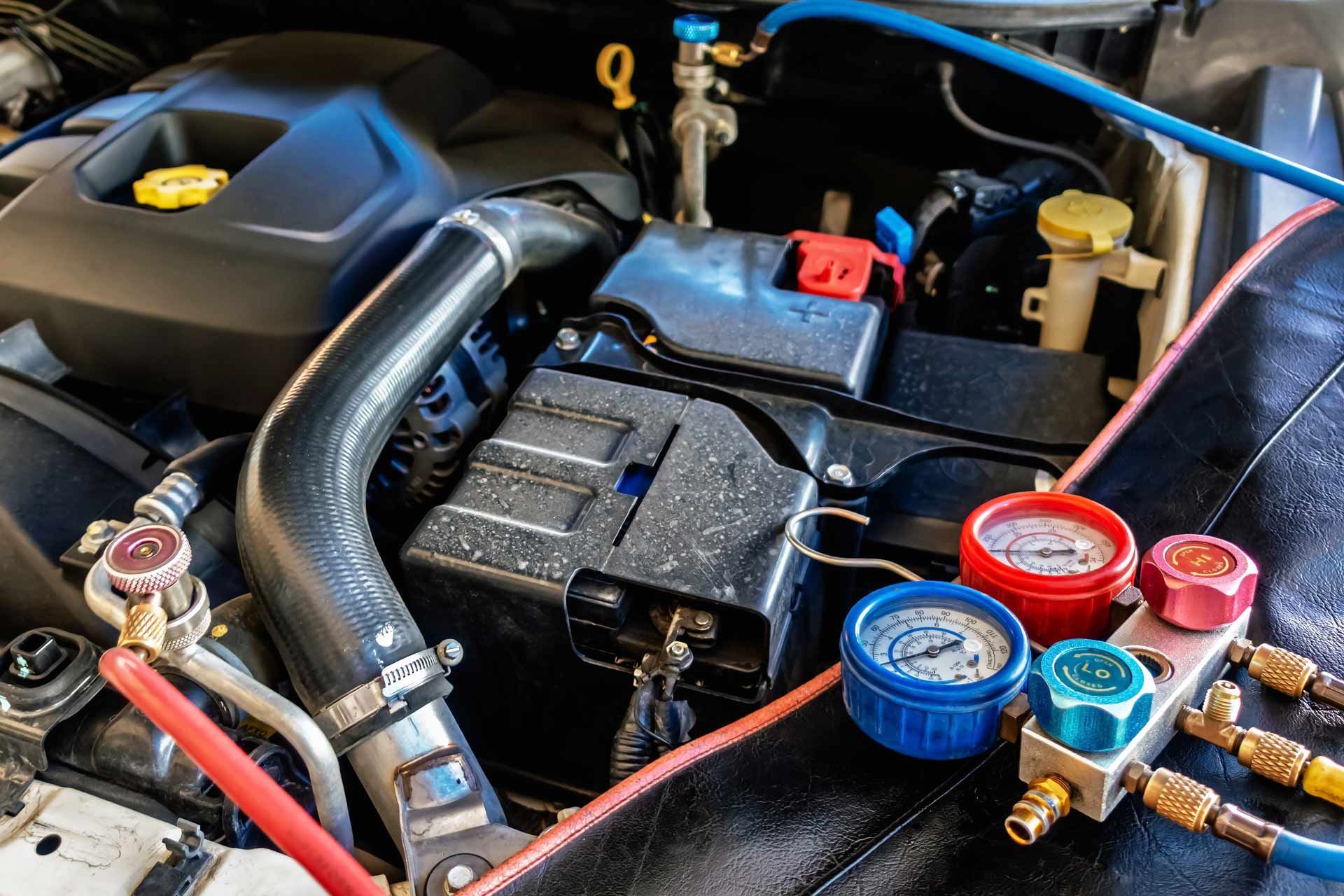 Car engine bay with battery, hoses, and colorful coolant service caps for AC lines