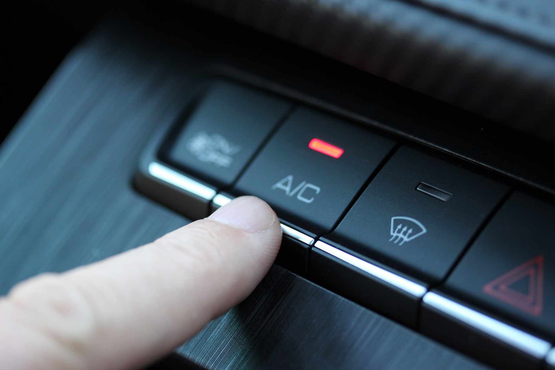 Finger pressing the A/C button on a car dashboard climate control panel