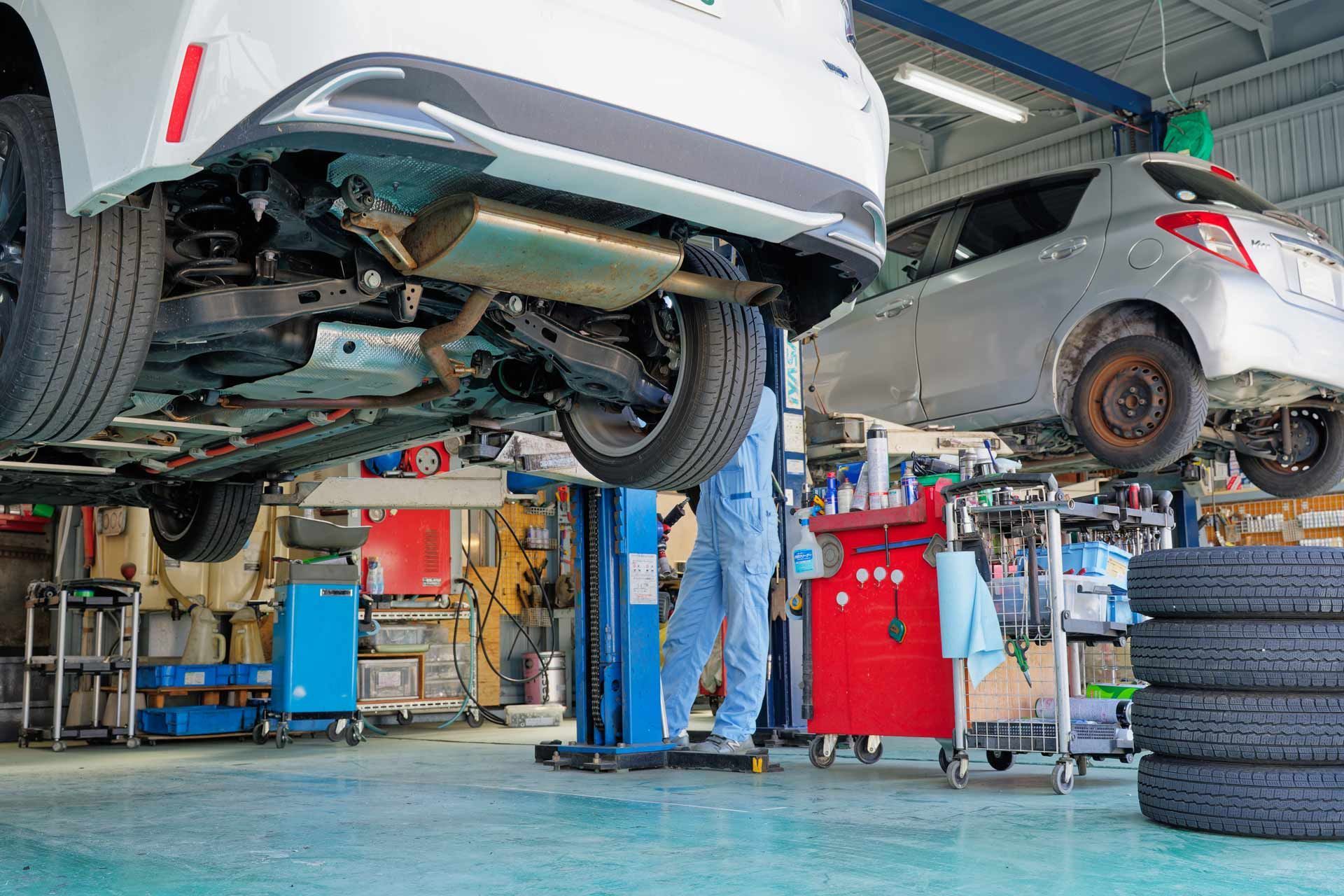 Cars being repaired in an auto shop, with mechanics working underneath on lifts and stacked tires nearby