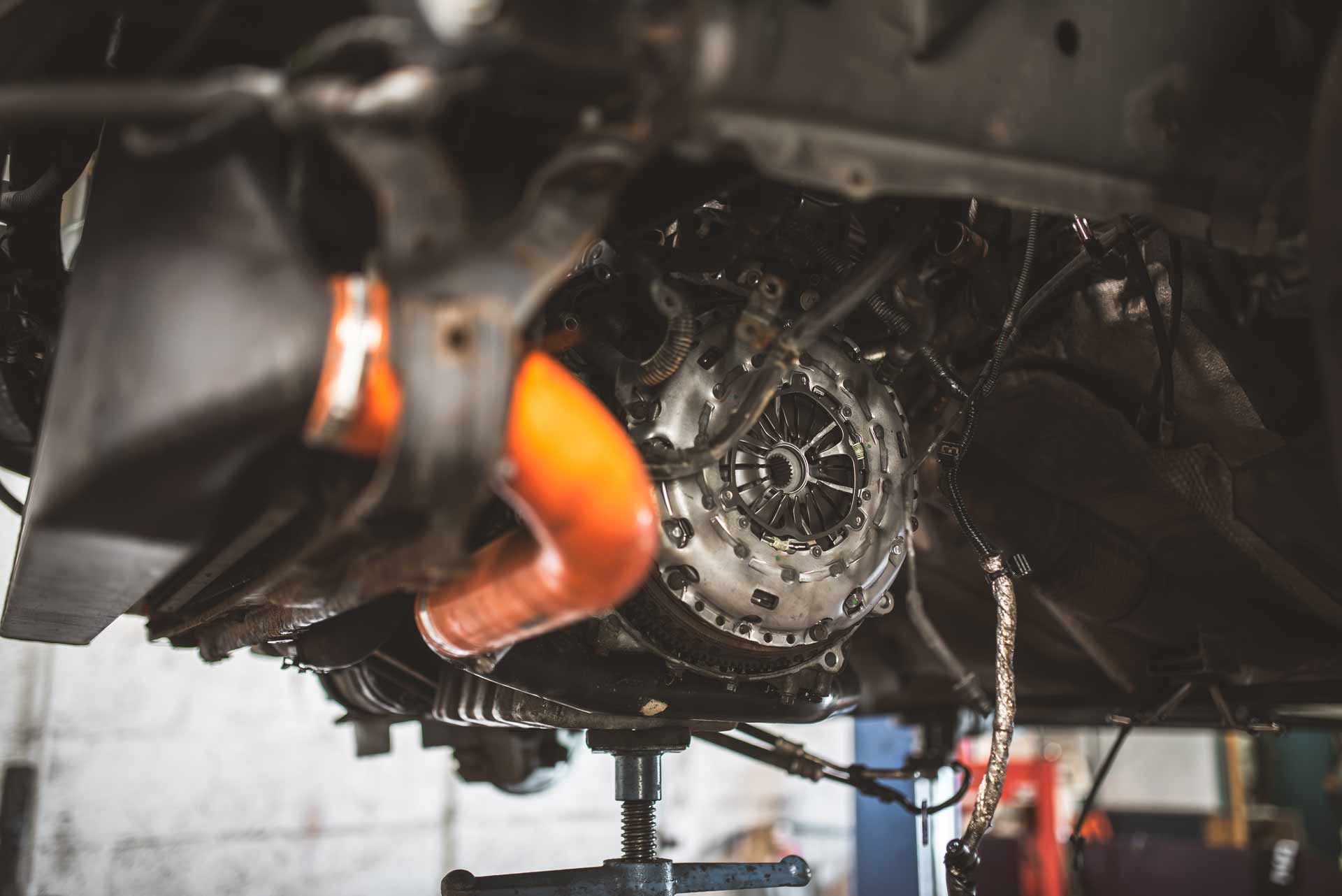 Close-up of a car’s exposed wheel hub and brake assembly in a repair shop, with an orange jack stand nearby