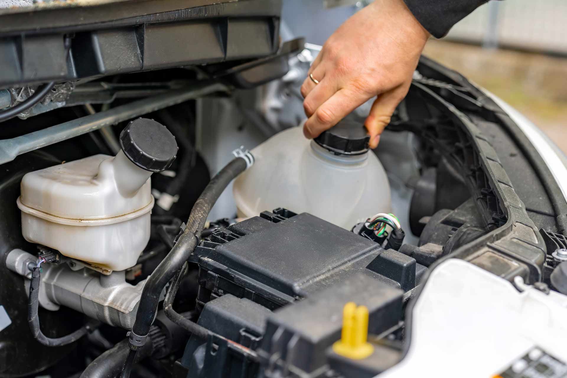 Hand pouring fluid into a car engine reservoir under the hood