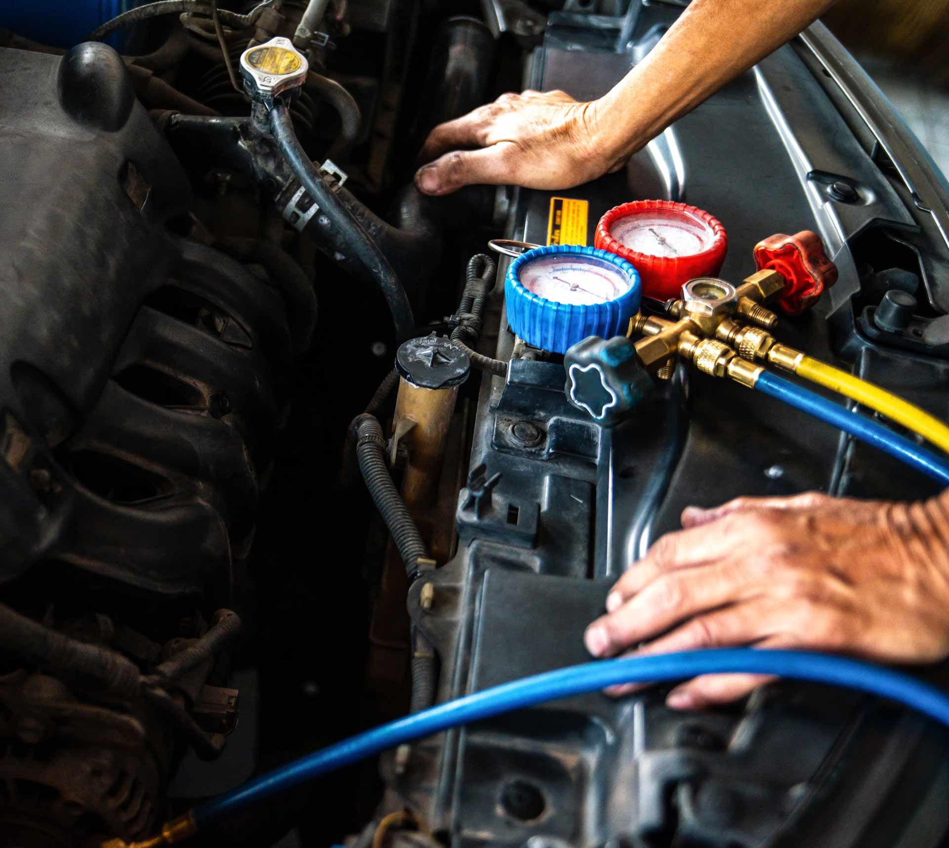 Mechanic using manifold gauges to service a car air conditioner in an engine bay