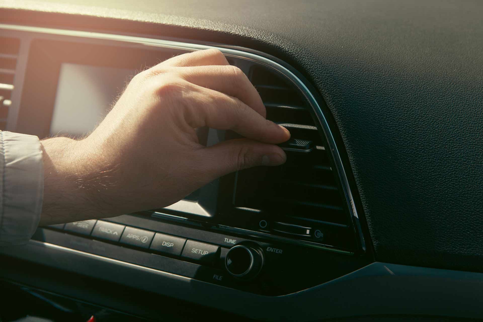 Hand turning the car’s air vent knob beside the dashboard in sunlight